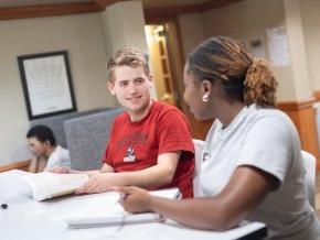 Two students look at each other while studying indoors